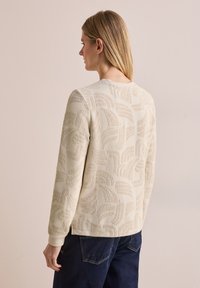 Beiger, gestrickter Pullover mit strukturiertem Blattmuster, gerippten Bündchen und rundem Ausschnitt. Die Rückansicht zeigt eine entspannte Passform und horizontale Nähte.