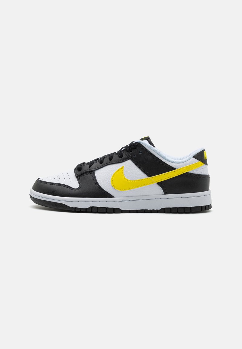 Baskets Nike Dunk Low avec une tige en cuir noir, une boîte à orteils blanche, un swoosh jaune et une semelle grise avec des accents noirs.