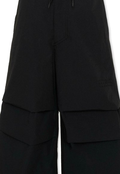 Pantalon noir à jambes larges avec des détails en tissu superposé sur les cuisses et un petit logo brodé sur la partie supérieure de la jambe droite.