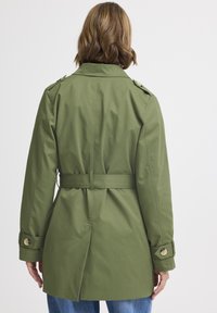 Trench coat verde con cintura, aperturas posteriori, spalline e polsini abbottonati. Realizzato in un tessuto liscio e resistente all'acqua.