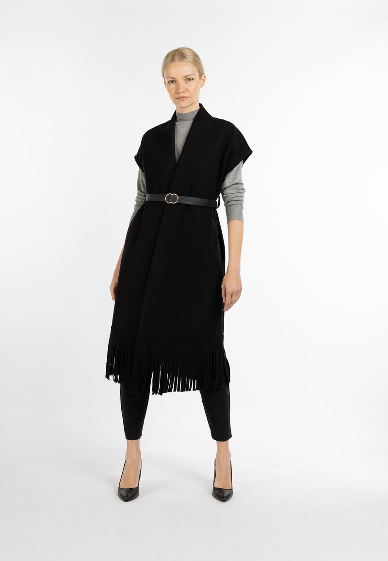 Zwarte franjenvest met een ceintuurlijf, gelaagd over een grijze top. Het model combineerde het met zwarte skinny jeans en zwarte hoge hakken.