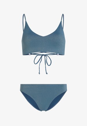 Mėlynas blizgus bikinio rinkinys, kuriame yra braletės tipo viršus su reguliuojamomis petnešėlėmis ir surišimu priekyje, derinamas su mažai kylantiems apatiniais.