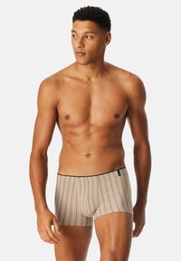 Beżowe bokserki w paski z czarną gumką, wykonane z gładkiego, elastycznego materiału. Posiadają konturowany krój kieszeni.