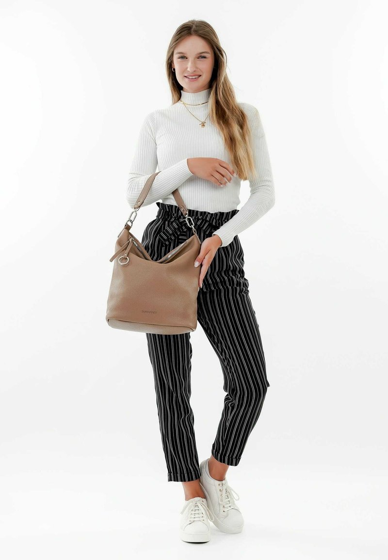 Sac en cuir marron à bandoulière avec un design décontracté, des accessoires en métal argenté et une seule sangle, associé à un pantalon rayé noir et blanc et des baskets blanches.