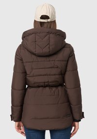 Bruine gewatteerde jas met capuchon, met een getailleerde taille, doorgestikt patroon en elastische manchetten. Een neutrale pet wordt er bij gedragen.