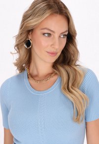 Top de punto acanalado azul claro con mangas cortas, que presenta un sutil patrón de trenzas. Un collar de cadena dorada y pendientes octagonales negros añaden contraste.