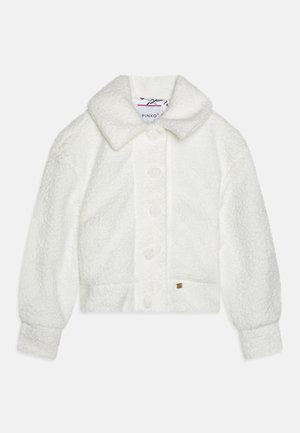 Λευκή κομμένη ζακέτα από αφράτο, υφασματικό ύφασμα. Διαθέτει ένα αιχμηρό γιακά, έξι μεγάλους κουμπιά και μια μικρή λογοτύπηση στο στρίφωμα.