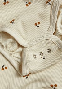 Crème kleurig geribbeld babyrompertje met kleine bruine kersenprint en drie drukknoopjes bij het kruis voor sluiting.