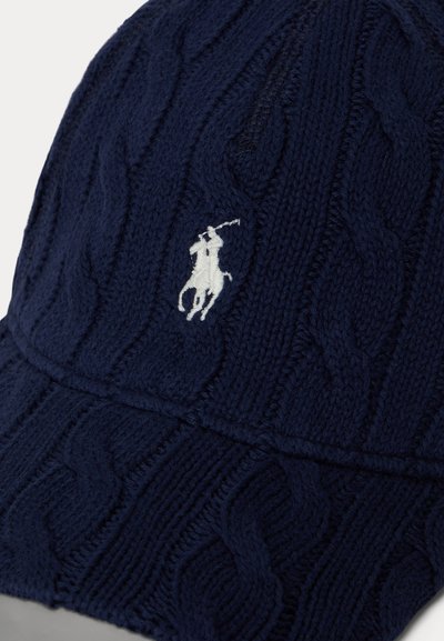 Μπλε σκούφος πλεκτός με σχέδιο καλωδίου, που έχει λευκό κεντημένο λογότυπο παίκτη πόλο στο μπροστινό μέρος.