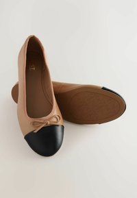 Beige ballerinat kengät mustalla varvasosalla ja pienellä nauhalla. Silkkinen muovimateriaali, jossa on litteä pohja ja teksturoitu pohja.