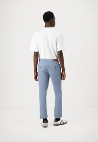 Pantaloni de un albastru deschis, dintr-un material moale, cu manșete rulate, buzunare spate cu detalii din buton, asortați cu un tricou simplu alb și adidași.