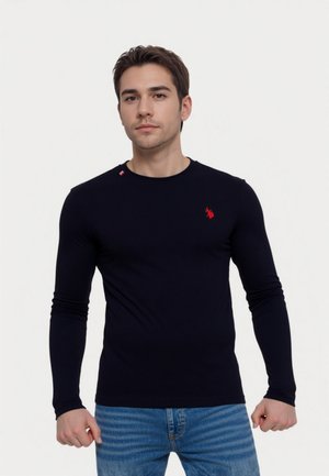 Marineblauwe longsleeve T-shirt gemaakt van katoen, met een slim fit design en een rood geborduurd logo op de borst en schouder. Draagt bij lichte spijkerbroek.
