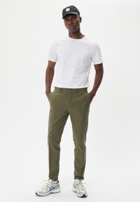Pantalones caqui con un corte ajustado, llevados con una camiseta blanca y una gorra negra. Acompañados de unas zapatillas de correr plateadas y azules.