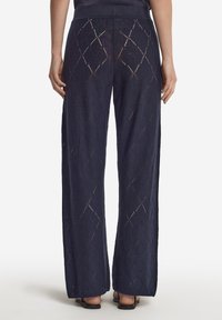 Marinblå vida byxor gjorda av en texturerad tyg med ett diamantmönstrat utskärningsdesign. Elastisk midja och avslappnad passform.
