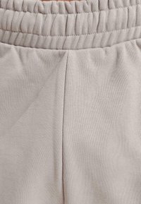 Lys beige joggebukser med en teksturert, elastisk linning og diskret søm. Har en avslappet passform og en glatt stofffinish.