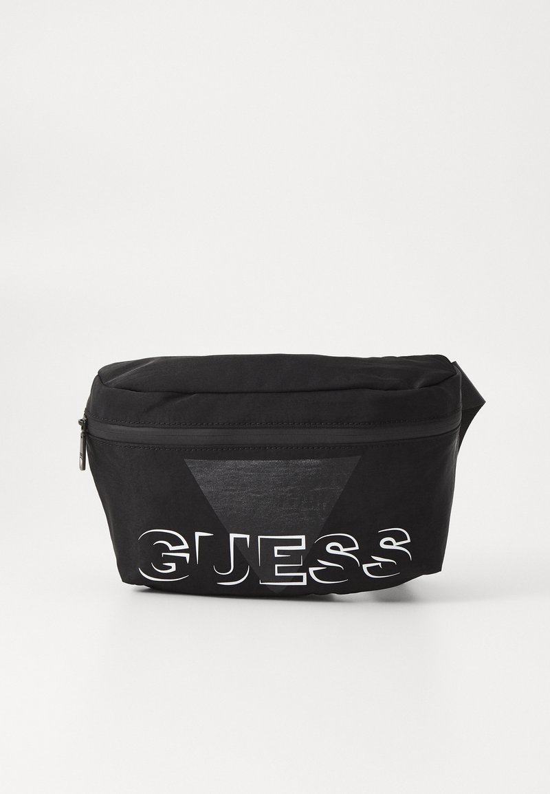 Mustaväri vyölaukku, jossa on sileä pinta, vetoketjukiinnitys ja suuri valkoinen "GUESS" -logo. Yhdellä sivulla on kolmiomainen muotoilu kontrastiksi.
