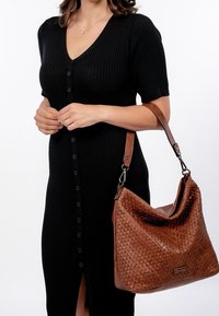 Czarna, prążkowana sukienka z krótkimi rękawami i zapięciem na guziki, w połączeniu z dużą brązową torebką skórzaną z plecionki, posiadającą regulowany pasek.
