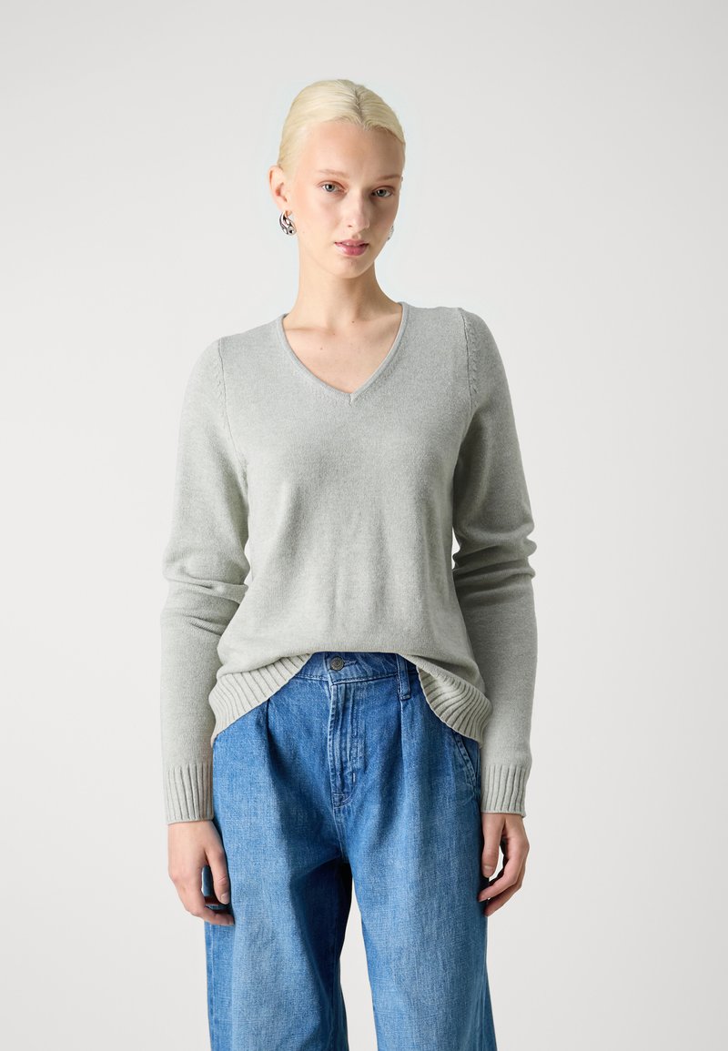 Maglione grigio chiaro a V in materiale morbido. Presenta polsini a costine e spacchi laterali. Abbinato a pantaloni di denim blu, comodi e larghi.