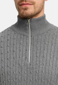 Grå, stickad tröja med kvartslång dragkedja och ribbad krage. Innehåller ett kabelstickat mönster och en silverfärgad dragkedja vid halslinningen.