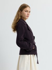 Giacca belted di colore viola scuro con colletto a revers e design doppiopetto. Tessuto liscio e strutturato, maniche lunghe con dettagli di bottoni.