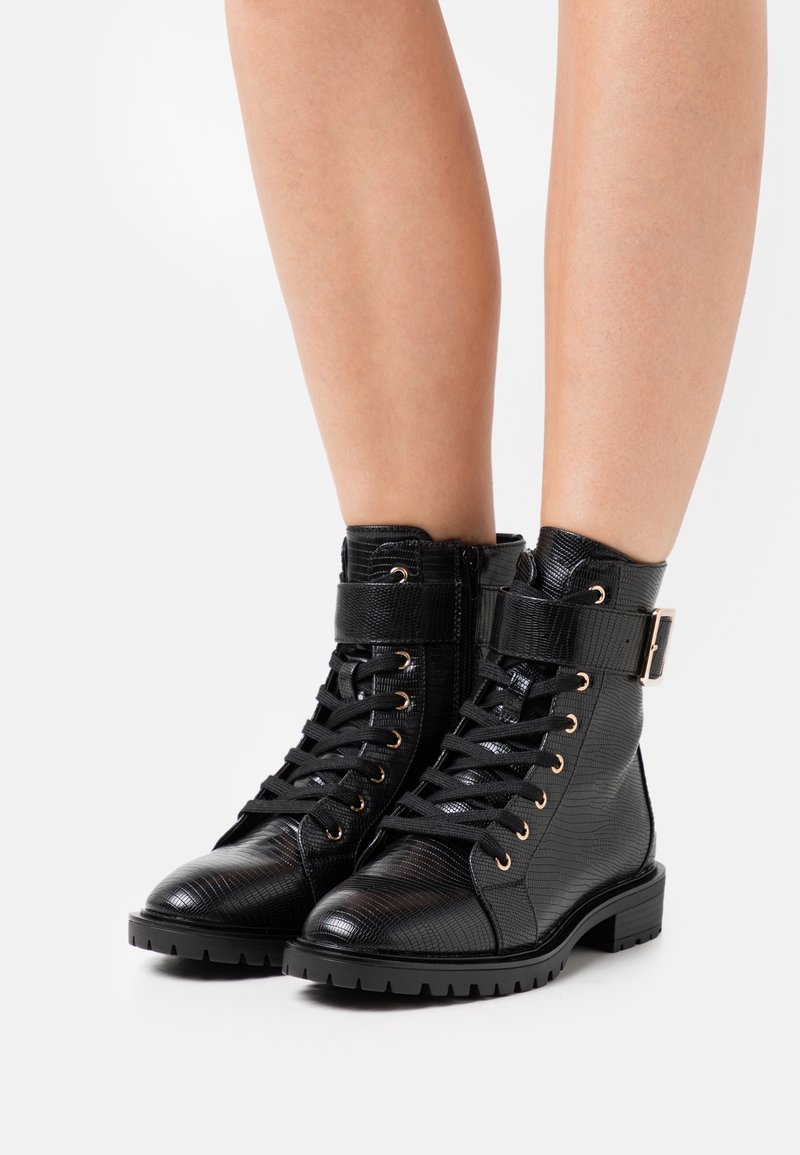 Bottines noires à lacets avec une finition texturée, des accessoires dorés et une bride à boucle. Dotées d'une semelle épaisse pour une meilleure adhérence.