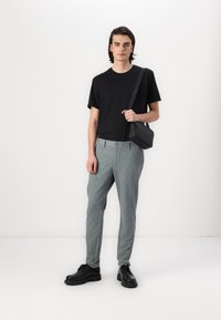 Black cotton t-shirt, gray checkered trousers, and black lace-up boots. Model carries a small black shoulder bag. Simple, minimalist design.