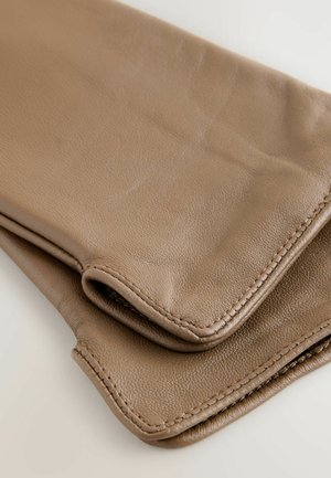 Gants en cuir marron doux, pliés, avec des coutures visibles sur un fond clair, montrant la texture et les coutures détaillées.