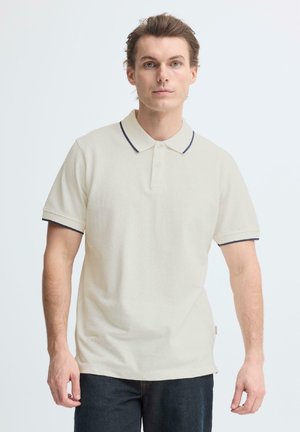 Beiges Poloshirt mit navyfarbenem Kragen und kurzen Ärmeln. Hergestellt aus strukturiertem Stoff, mit drei Knöpfen am Hals.