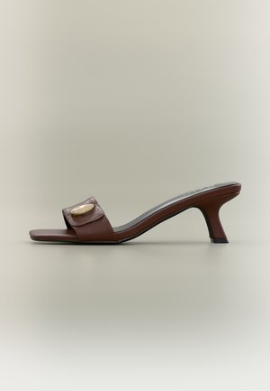 Bruine leren open-teen mule met een lage, gebogen hak en een brede band met een gouden decoratief accent.