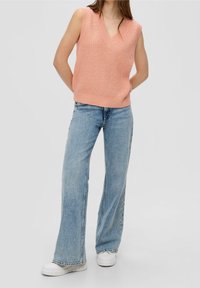 Top smanicato di maglia rosa chiaro con scollatura a V, abbinato a jeans a zampa d'elefante blu chiaro e sneakers bianche con plateau.