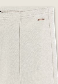 Tissu gris clair avec une texture douce et lisse. Présente des détails de couture subtils et une petite plaque métallique de marque.