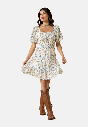 Bloemenprint mini-jurk in crèmekleur met pofmouwen, geplooide bustier en uitlopende rok. Gecombineerd met bruine cowboylaarzen.