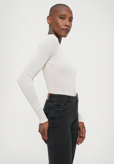 Long-sleeve white top in a fitted design, paired with high-waisted black jeans featuring side pockets and a textured finish.