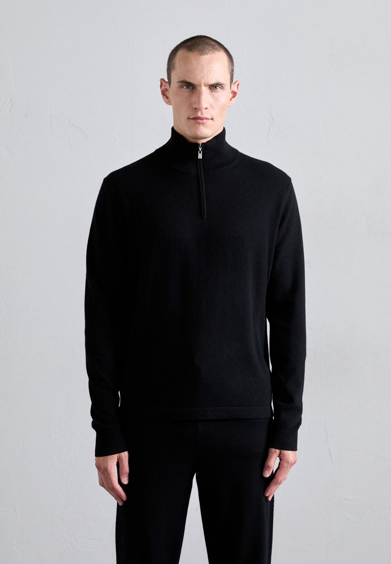 Schwarzer Pullover mit Reißverschluss am Hals, aus weichem Stoff gefertigt, mit langen Ärmeln und figurbetontem Schnitt. Minimalistisches Design mit einer eleganten Silhouette und subtiler Textur.