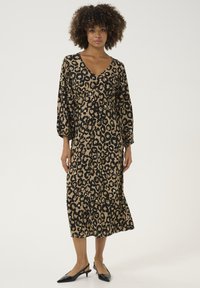Midi haljina s printom leoparda u bež i crnoj boji, s V-izrezom, nabranim strukom i dugim napuhanim rukavima. Uparena s crnim slingback potpeticama.
