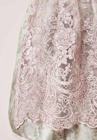 Delicaat roze bloemenkant overlay met ingewikkelde borduursels en pailletten op een lichte bloemenpatroonstof eronder.