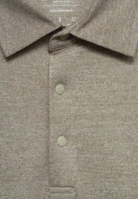 Polo shirt marrone con texture, colletto, tre bottoni e un leggero motivo heather. L'etichetta riporta "Performance."