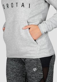 Felpa grigia con scritte nere e tasche, abbinata a leggings neri con un motivo testurizzato e inserti in rete.