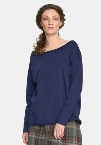 Granatowa bluzka z długim rękawem, z szerokim dekoltem w łódkę i luźnym krojem, wykonana z miękkiego materiału. Noszona z woskową spódnicą.