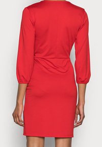 Robe rouge ajustée avec manches longues bouffantes, en tissu lisse. Dispose d'une taille cintrée et d'un ourlet droit. Détails minimaux.
