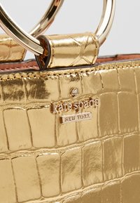 Borsa metallizzata dorata con texture a coccodrillo, dotata di una placca con logo e manici circolari in metallo. Finitura liscia e cuciture a vista.