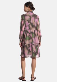 Abito leggero e trasparente con un motivo astratto multicolore in rosa, verde e marrone. Presenta maniche lunghe, colletto e un orlo a balze.