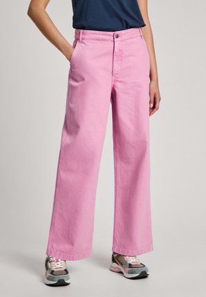Rosafarbene, weit geschnittene Jeans aus glattem Baumwollmaterial, mit Taschen und einem Knopfverschluss. Kombiniert mit mehrfarbigen Turnschuhen.
