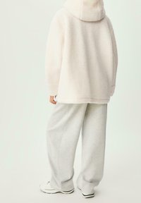 Zachte, lichtroze gewatteerde jas met capuchon en losse pasvorm, gecombineerd met grijze joggingbroek en witte sneakers. Zachte textuur en casual ontwerp.