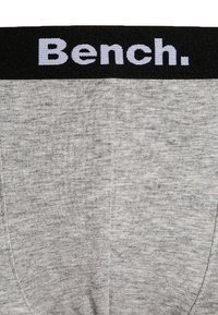 Szürke pamut alsó, fekete elasztikus derékpánttal, amelyen világoslila színnel van írva a "Bench." A textúrája puha, felülete sima.