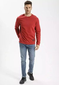 Czerwona bawełniana bluza z okrągłym dekoltem, ściągaczami przy mankietach i u dołu. Połączona z niebieskimi dżinsami i czarnymi trampkami. Prosty design bez wzorów.