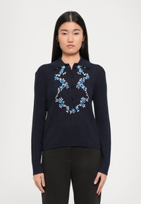 Navy pulovrová mikina s žebrovanou texturou a límečkem, zdobená bílou a modrou květinovou výšivkou přes hruď a se třemi knoflíky.