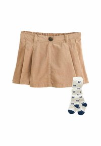 Hellbeige Cord-Ripprock mit Falten und Knopfverschluss, kombiniert mit weißen Socken, die ein blaues Schleifenmuster und blaue Spitzen haben.