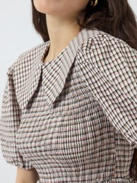 Multicolored checkered blouse featuring a large collar, puffed sleeves, and gathered texture. Fabric combines tones of pink, brown, and white.