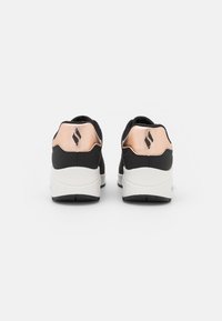 Scarpe da ginnastica nere con un accento in rosa oro sul tallone, caratterizzate da una superficie testurizzata e una suola intermedia bianca. Logo visibile su ogni tallone.